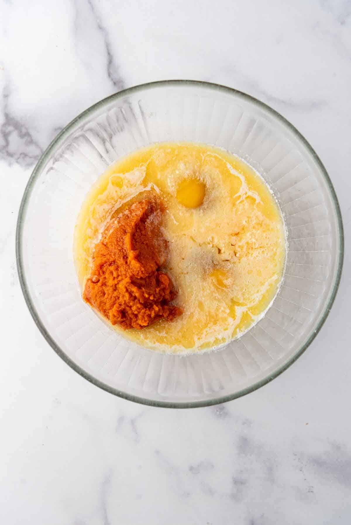 Ingrédients humides pour le pain de maïs à la citrouille dans un bol de mélange en verre.