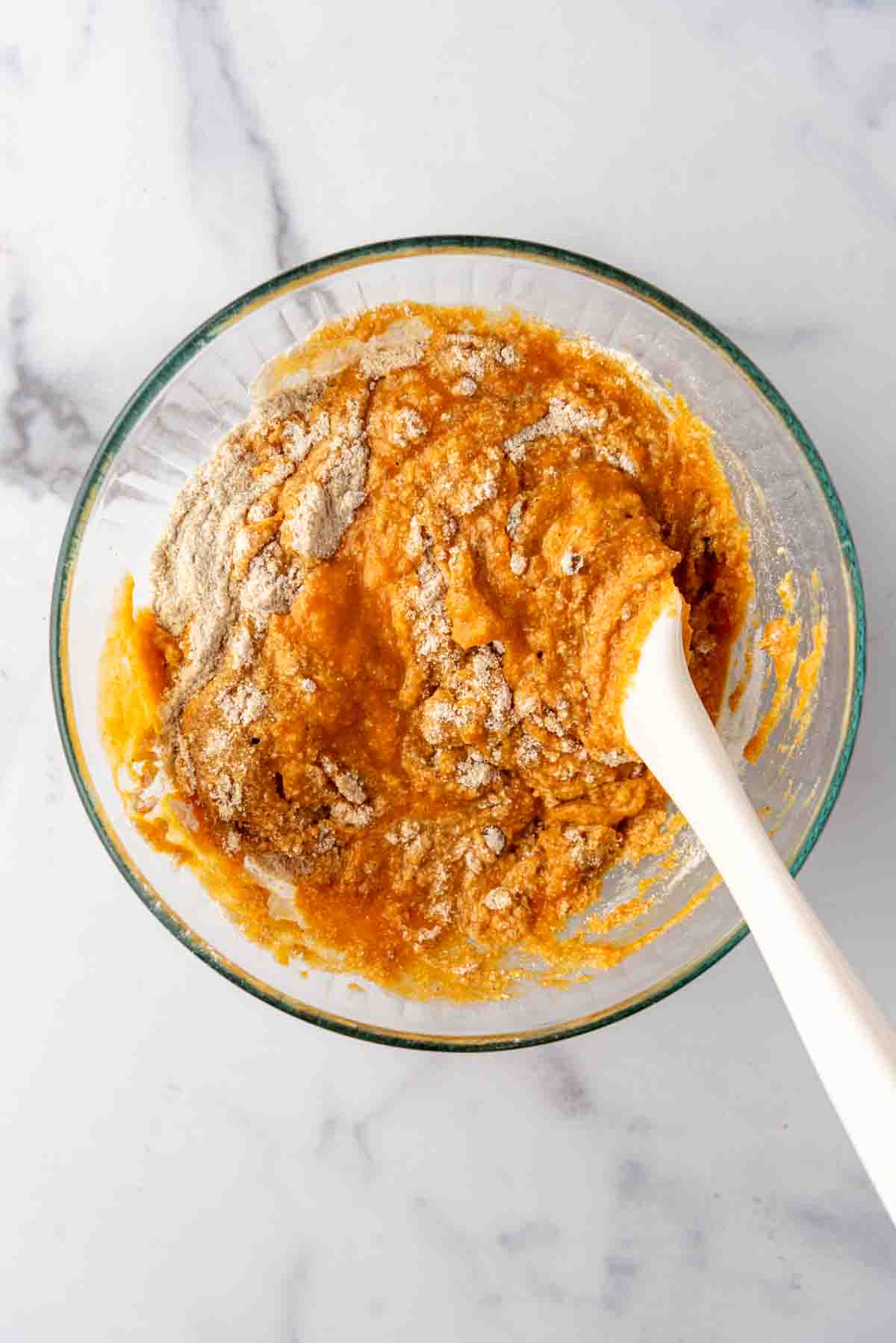 Combining wet and dry ingredients in a glass mixing bowl with a spatula.