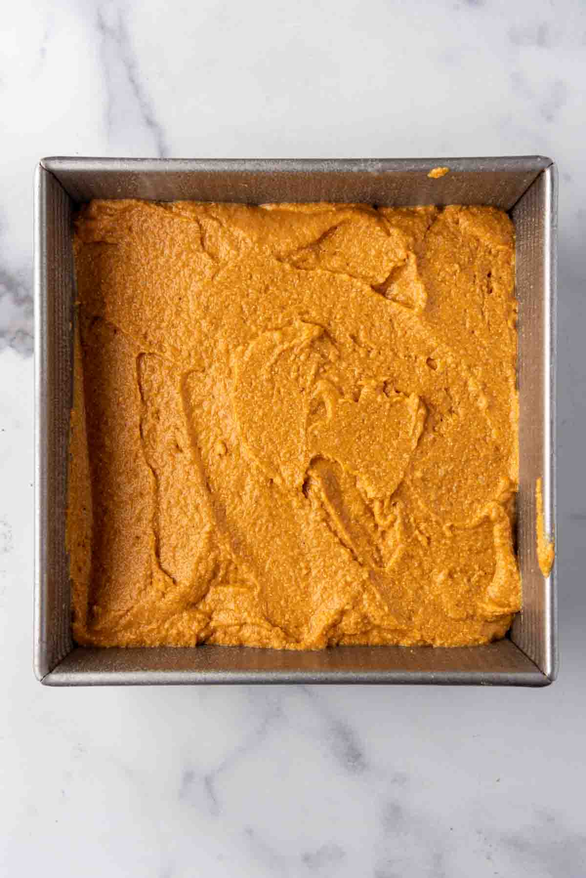 Pumpkin cornbread batter in a square baking pan.