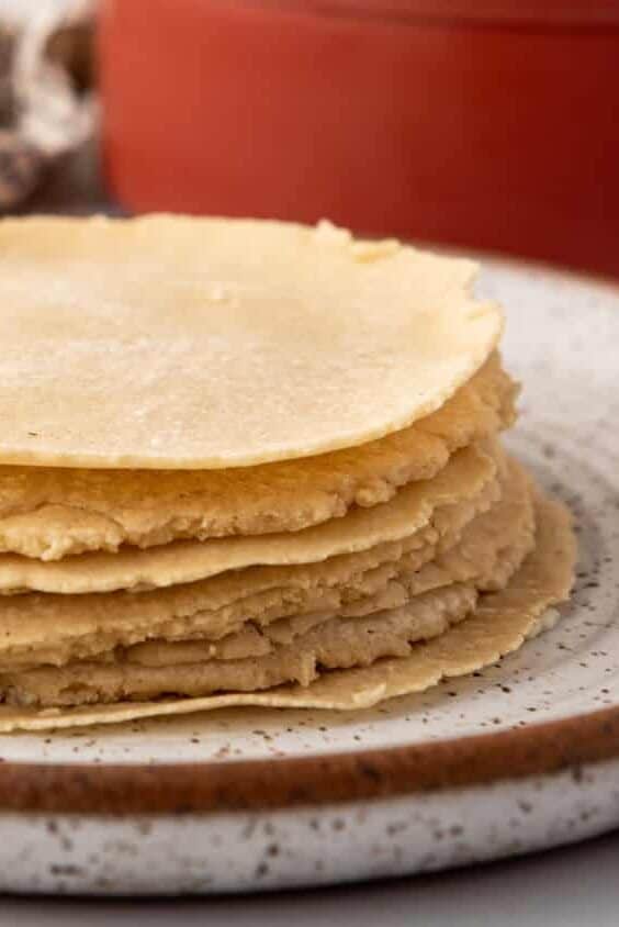 An image of homemade corn tortillas stacked on a plate.