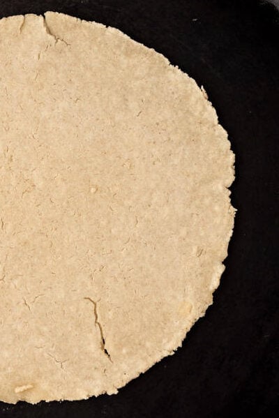 An overhead image of a corn tortilla being cooked in a cast iron skillet.