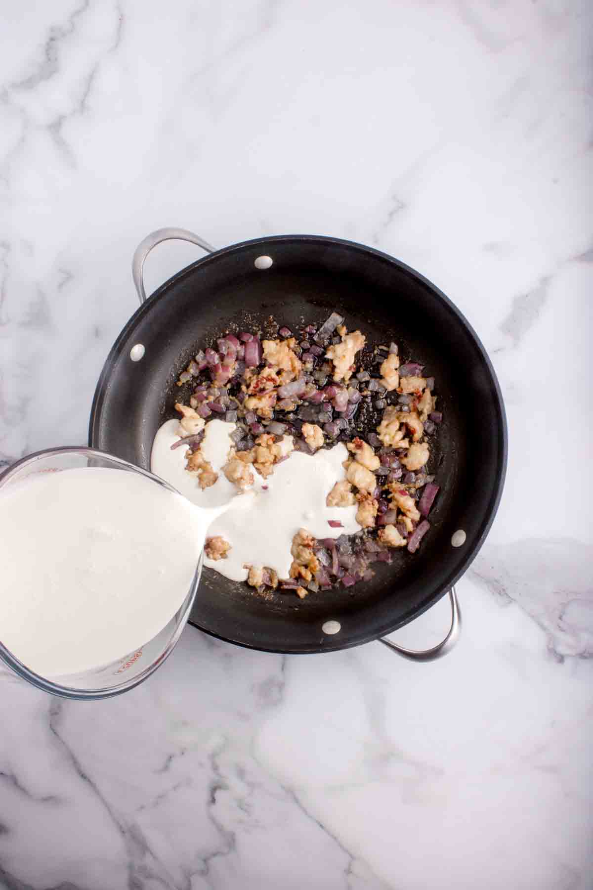 Adding heavy cream to a pan of other ingredients.