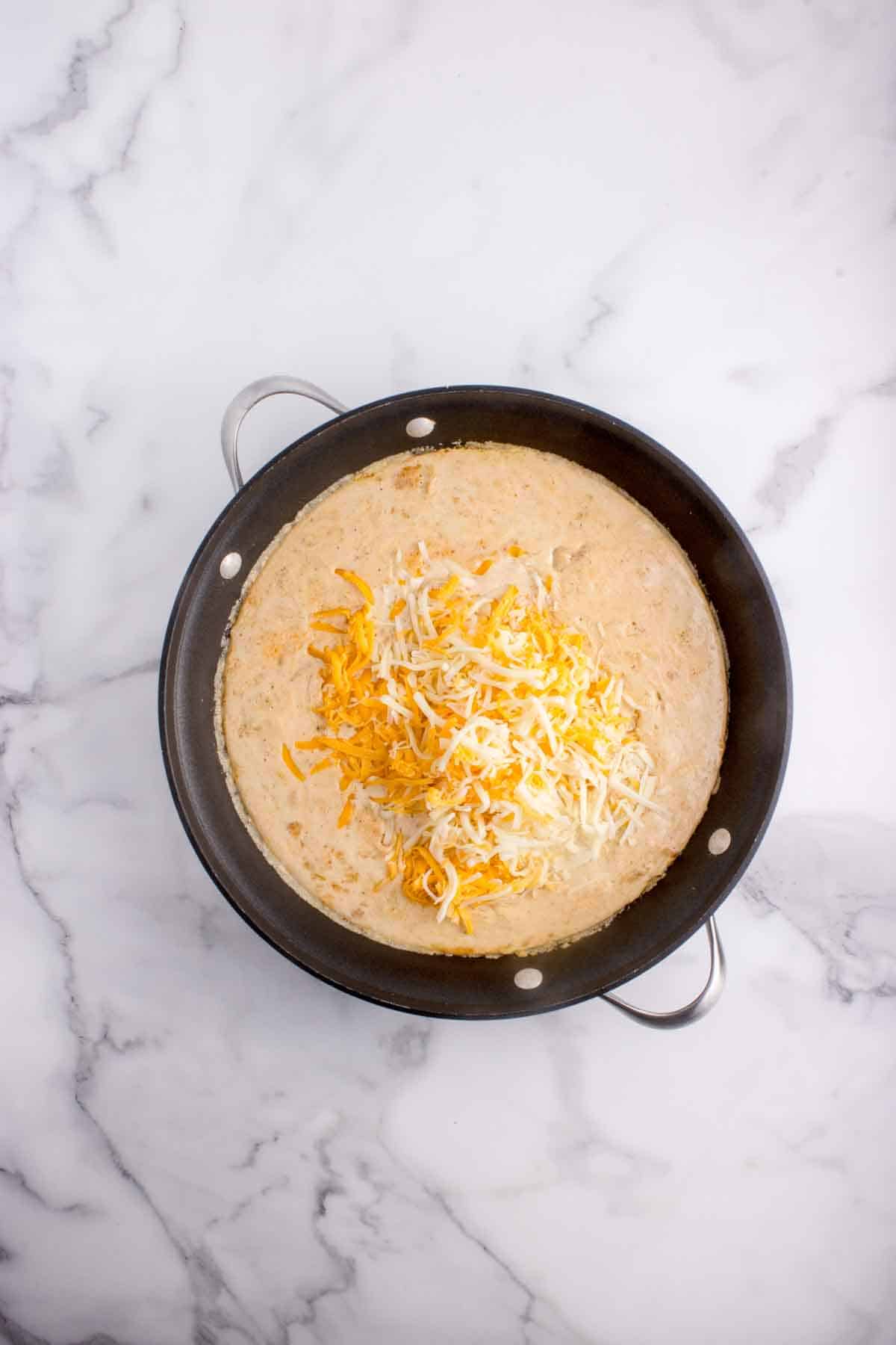 Adding shredded cheese to make a sauce for mac and cheese.