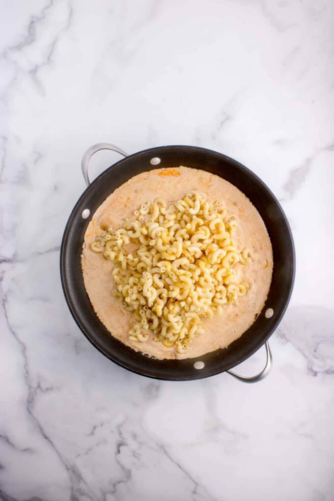 Adding cooked and drained macaroni noodles in a cheese sauce.