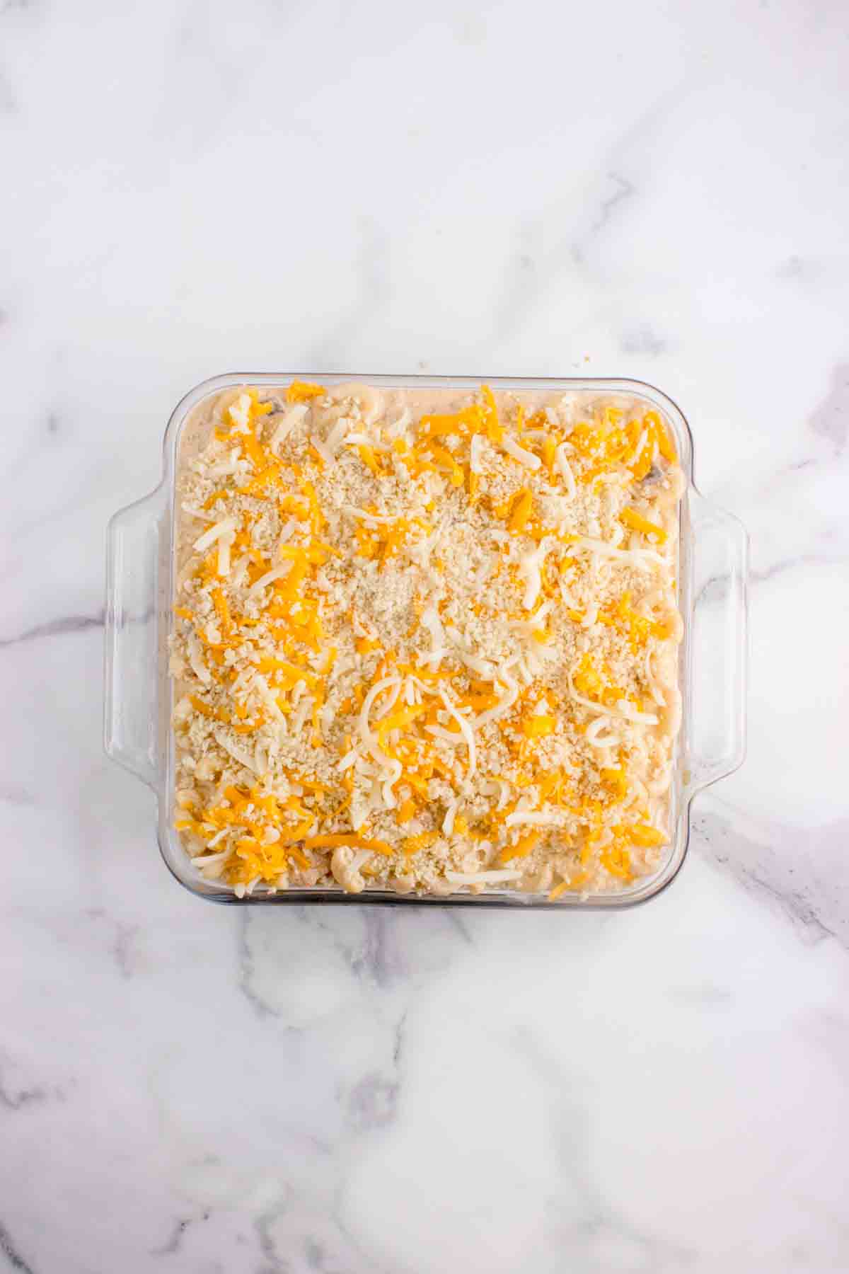 Adding shredded cheese and panko breadcrumbs on top of a pan of lobster mac and cheese.