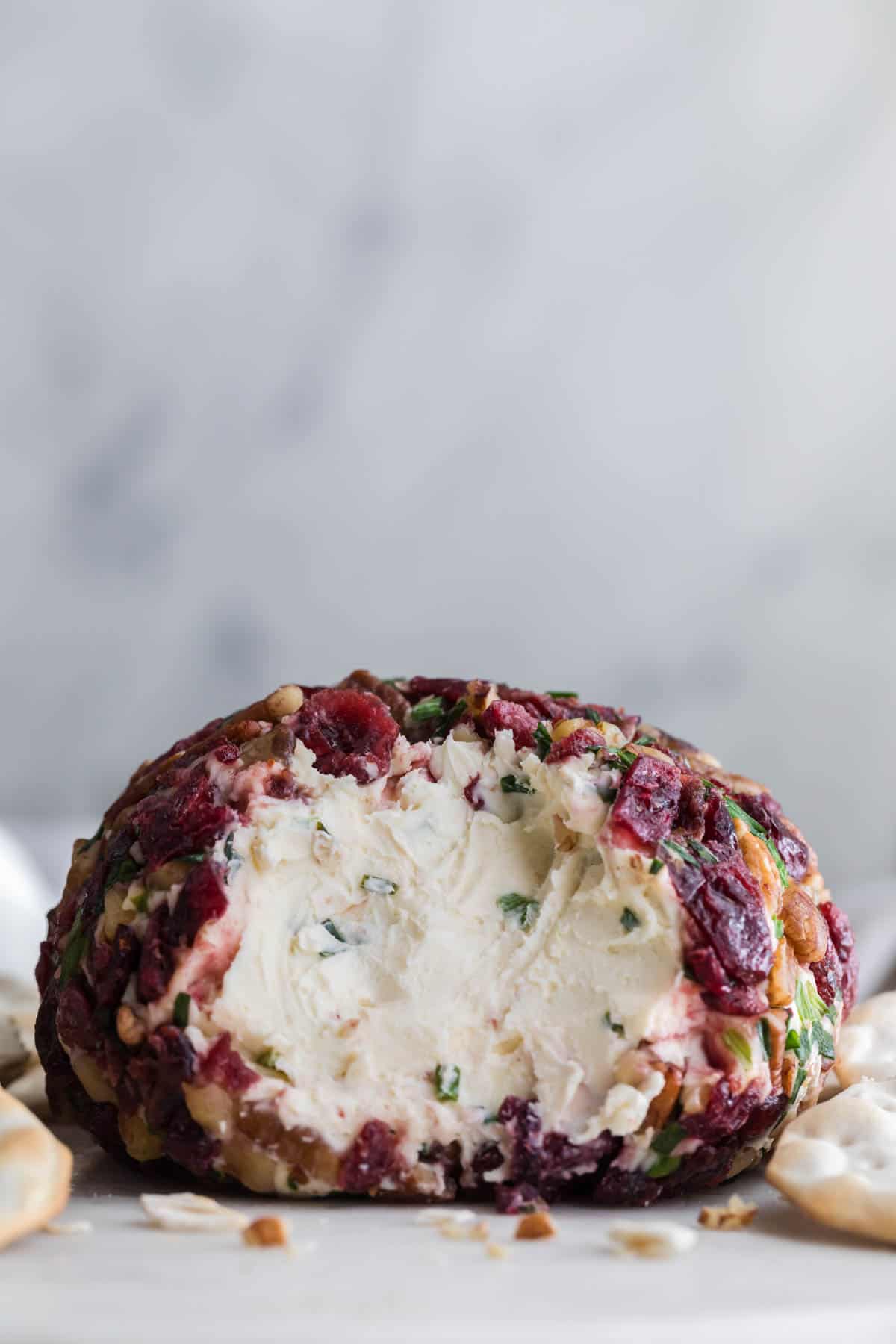 An image of a cranberry pecan cheeseball with part of it scooped out.