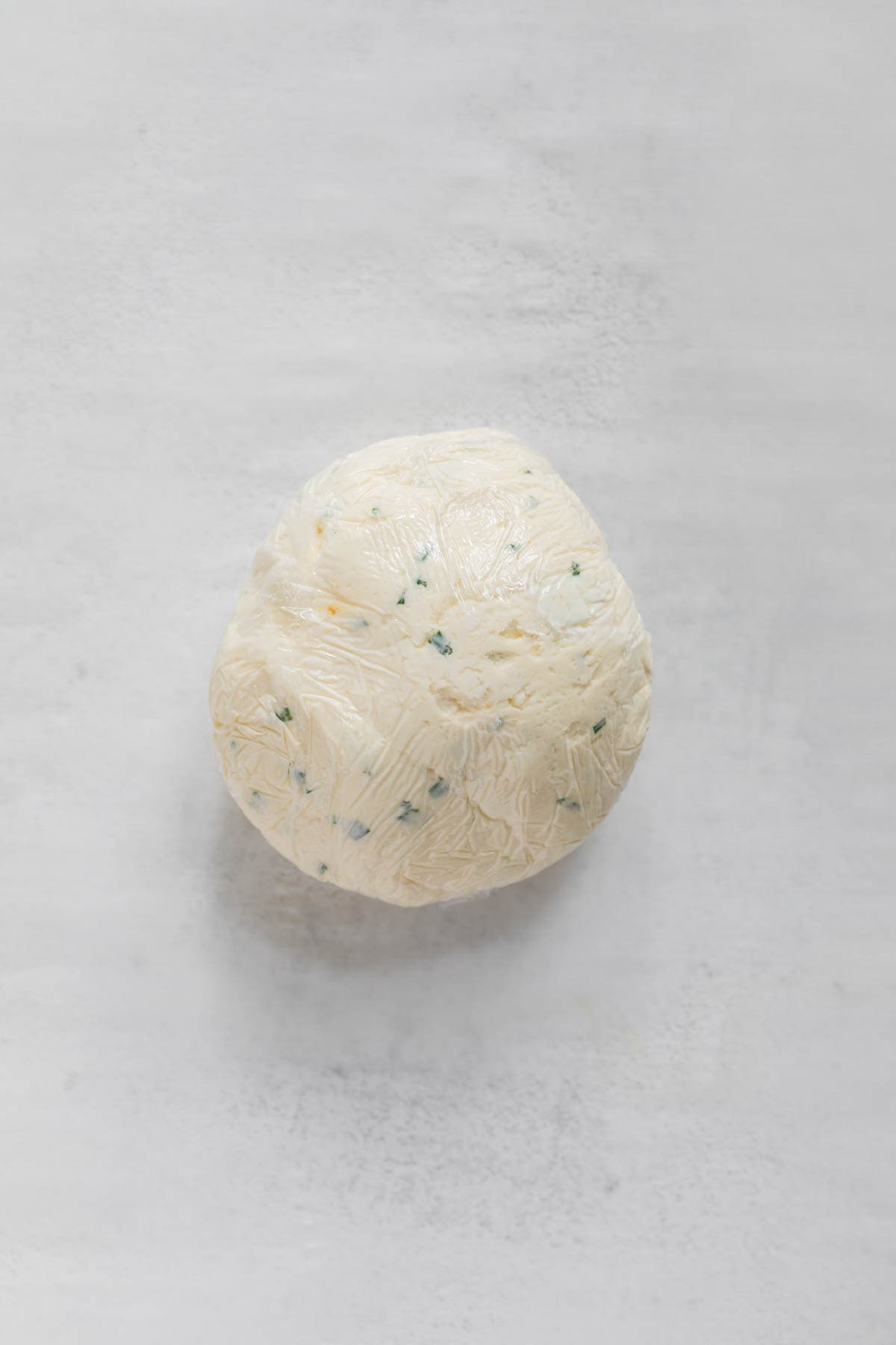 A wrapped and chilled cheeseball before being rolled in toppings.