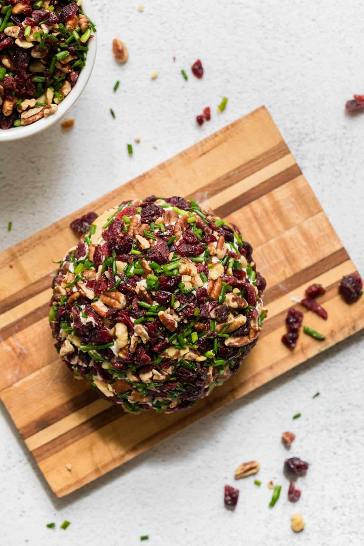 An overhead image of a cheeseball on a wooden cutting board.