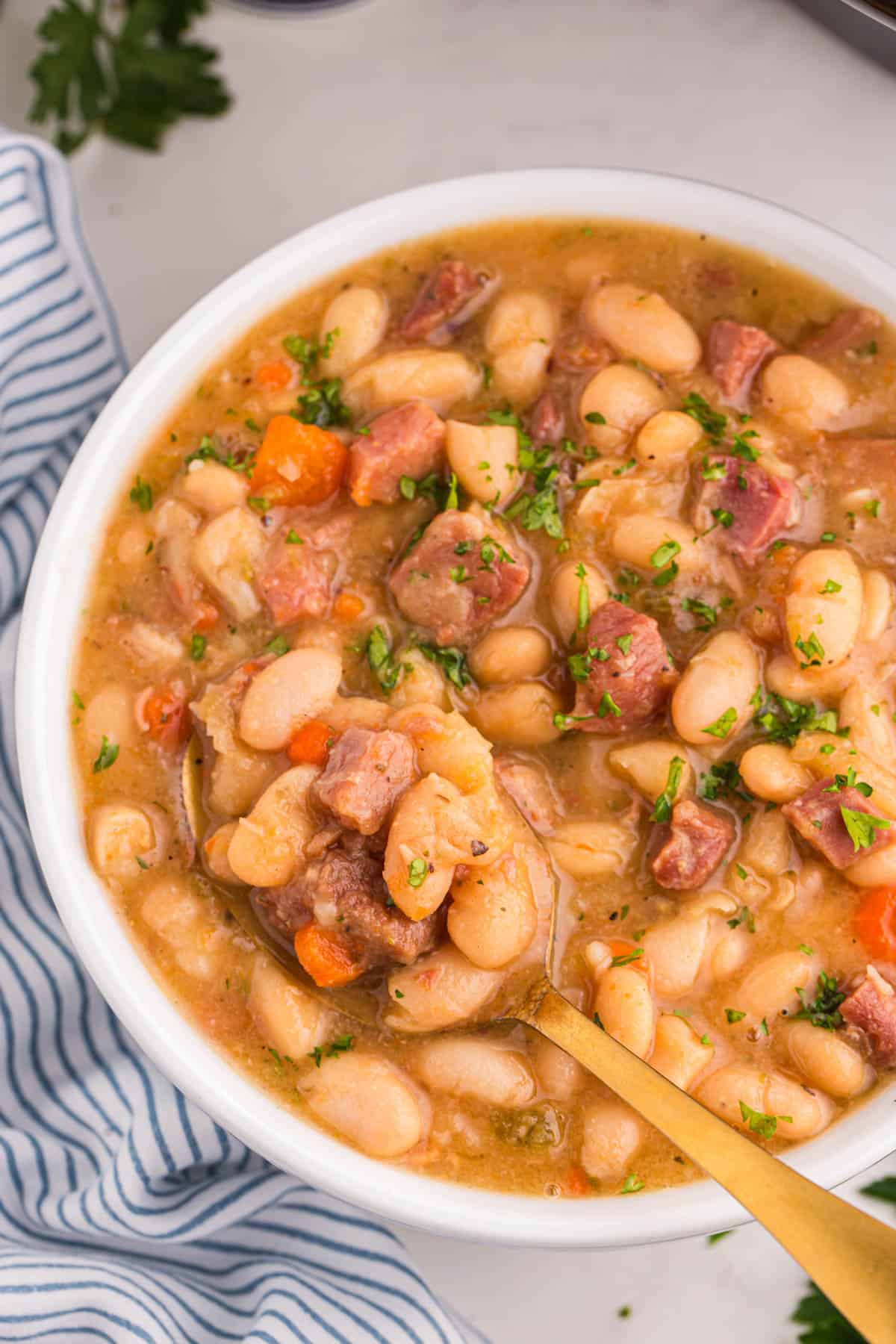 An overhead image of a bowl of crock pot ham and bean soup with a spoon in it.