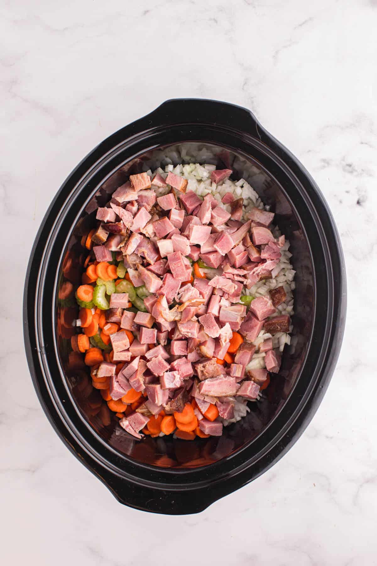 Adding chopped vegetables and ham to a crock pot.