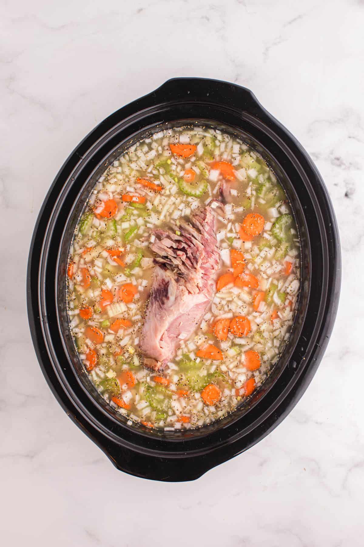 Adding liquid and a ham bone to a crock pot.