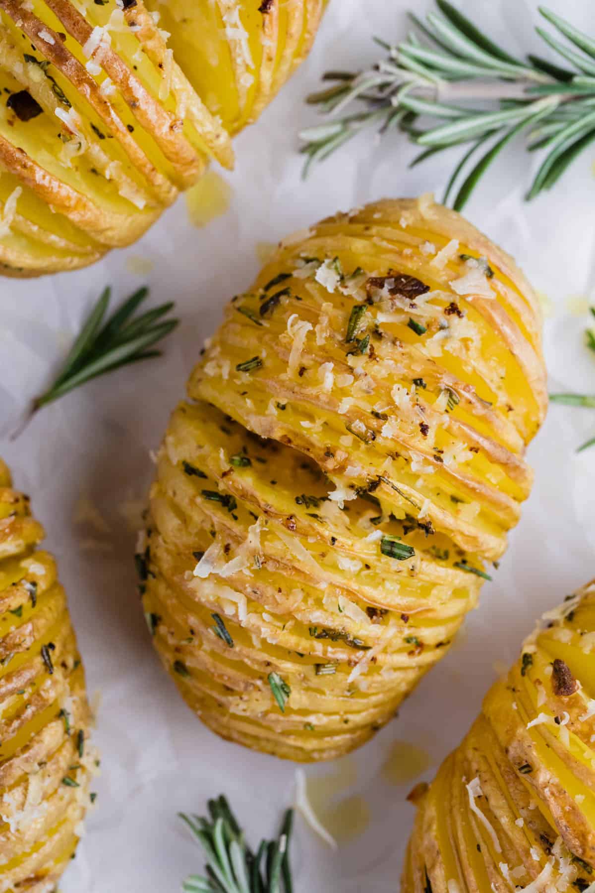 An overhead image of a hasselback potatoes surrounded by sprigs of rosemary.