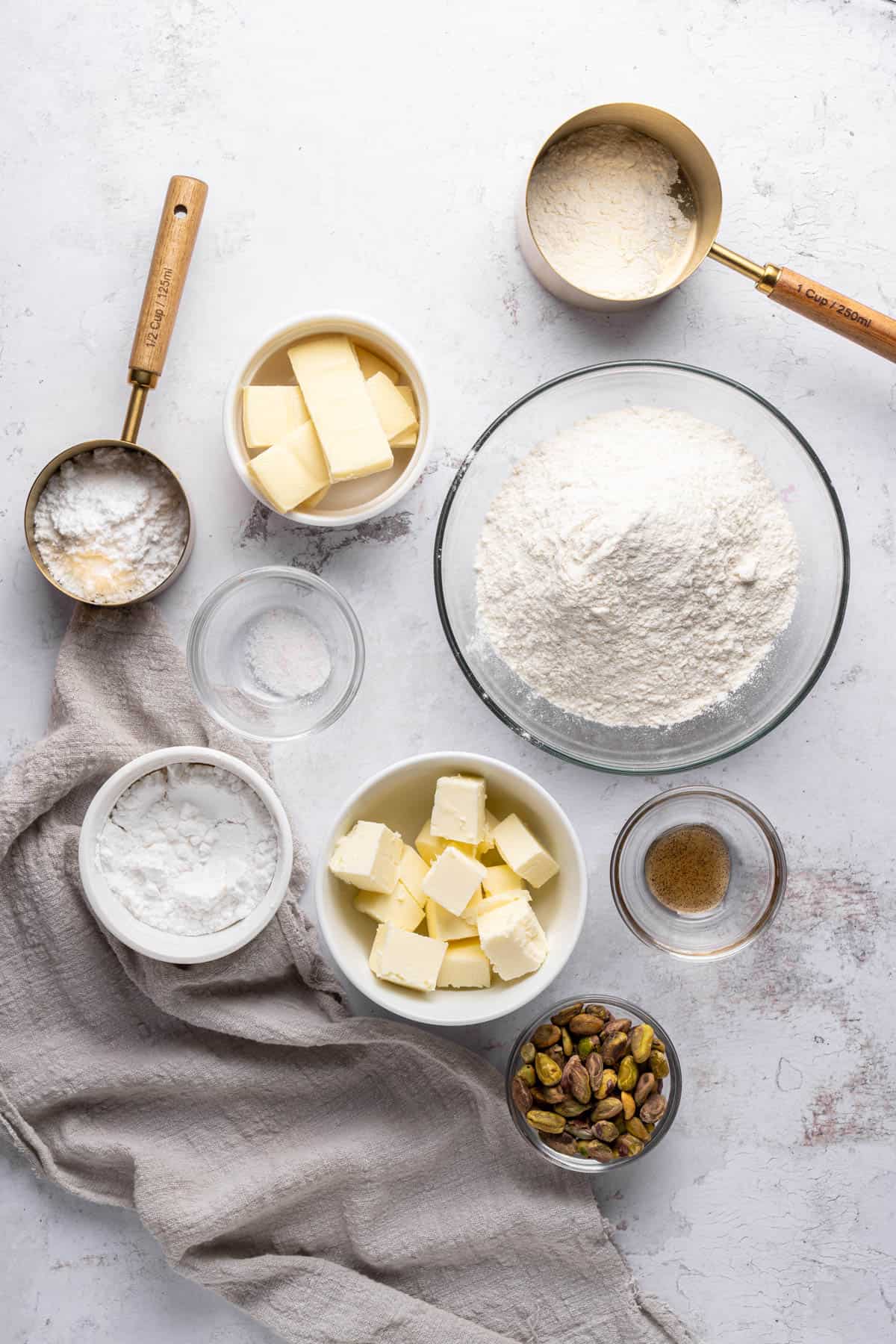 Overhead view of ingredients needed to make pistachio shortbread cookies in small bowls on a baking tray.