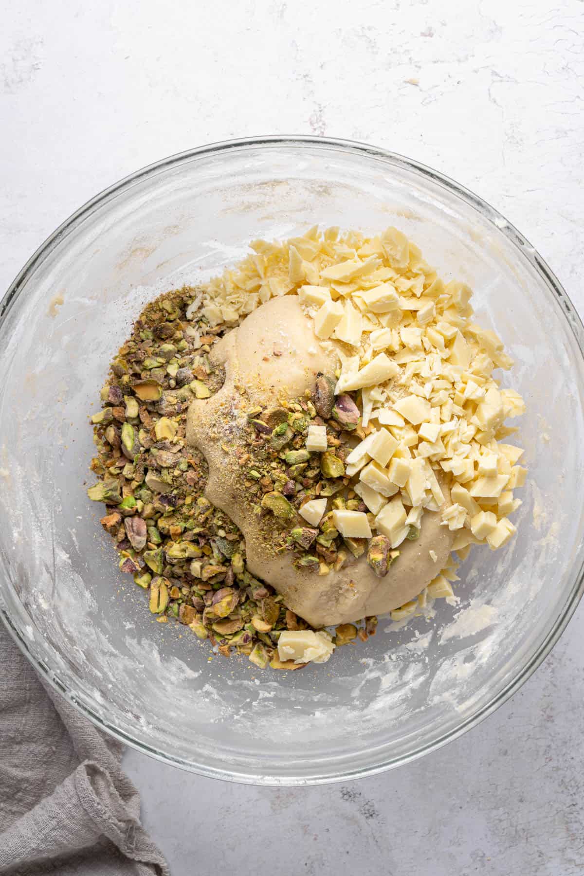 Overhead view of cookie dough mixture with chopped pistachios and white chocolate added to it in a large bowl.