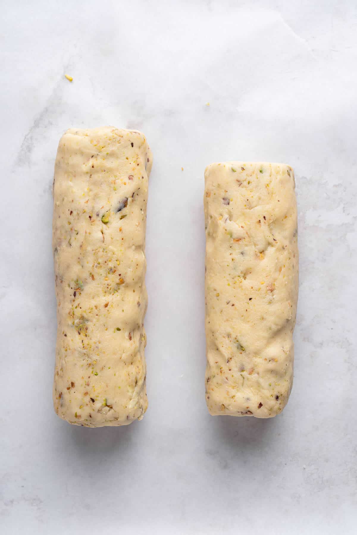 Overhead view of two logs of Pistachio Shortbread cookie dough on a white surface.