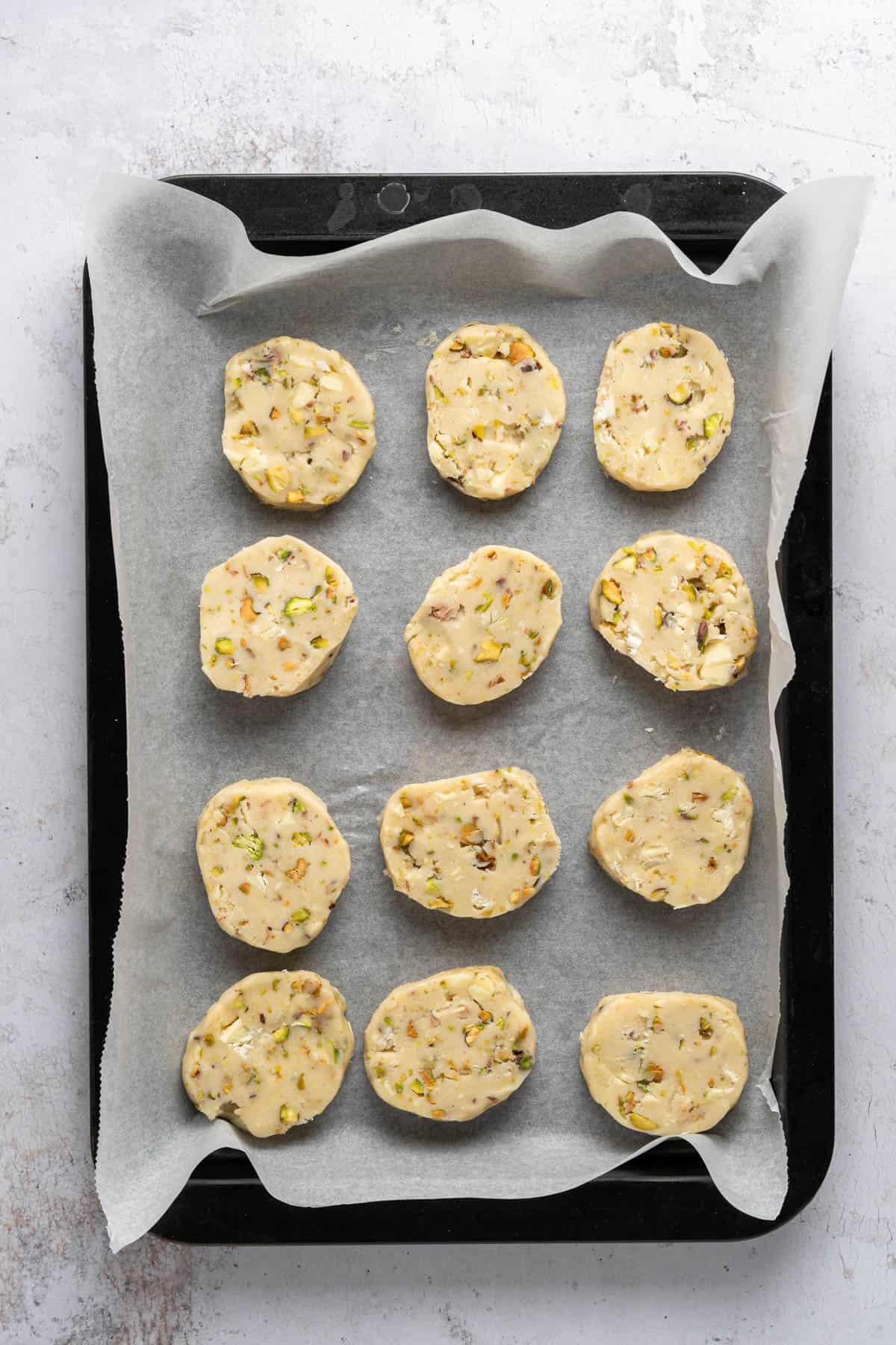 Overhead view of unbaked Pistachio Shortbread cookies on a parchment-lined baking tray.