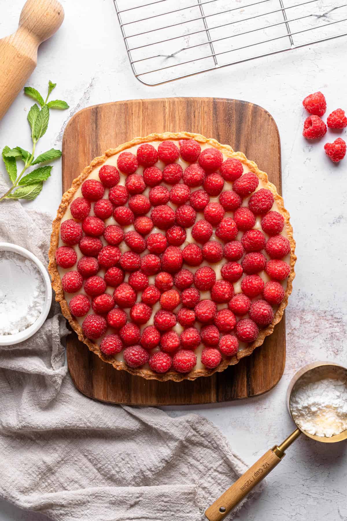 An image of a tart on a wooden cutting board with fresh raspberries on top.