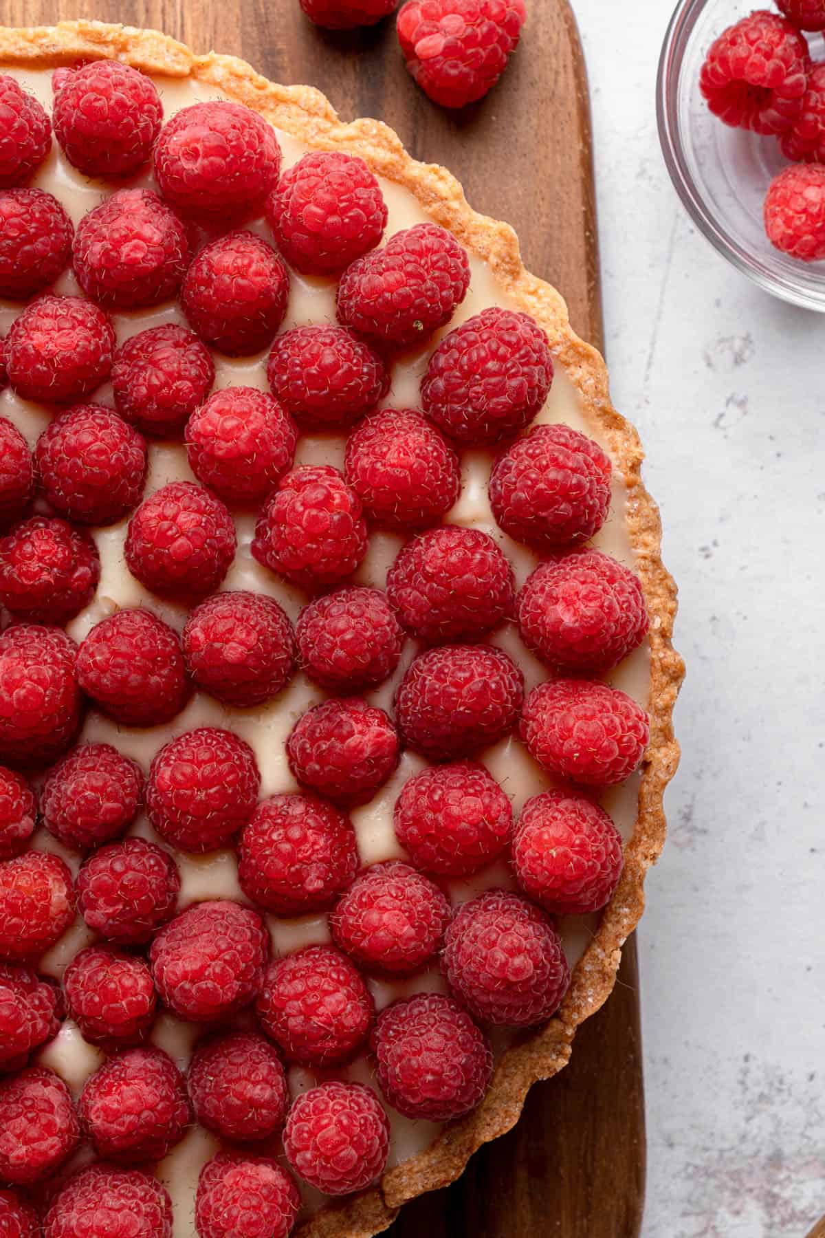 A close up image of a raspberry tart on a wooden cutting board.