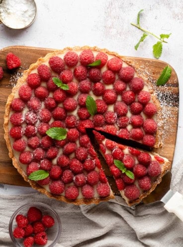 An overhead image of a raspberry chocolate tart with a slice being removed.