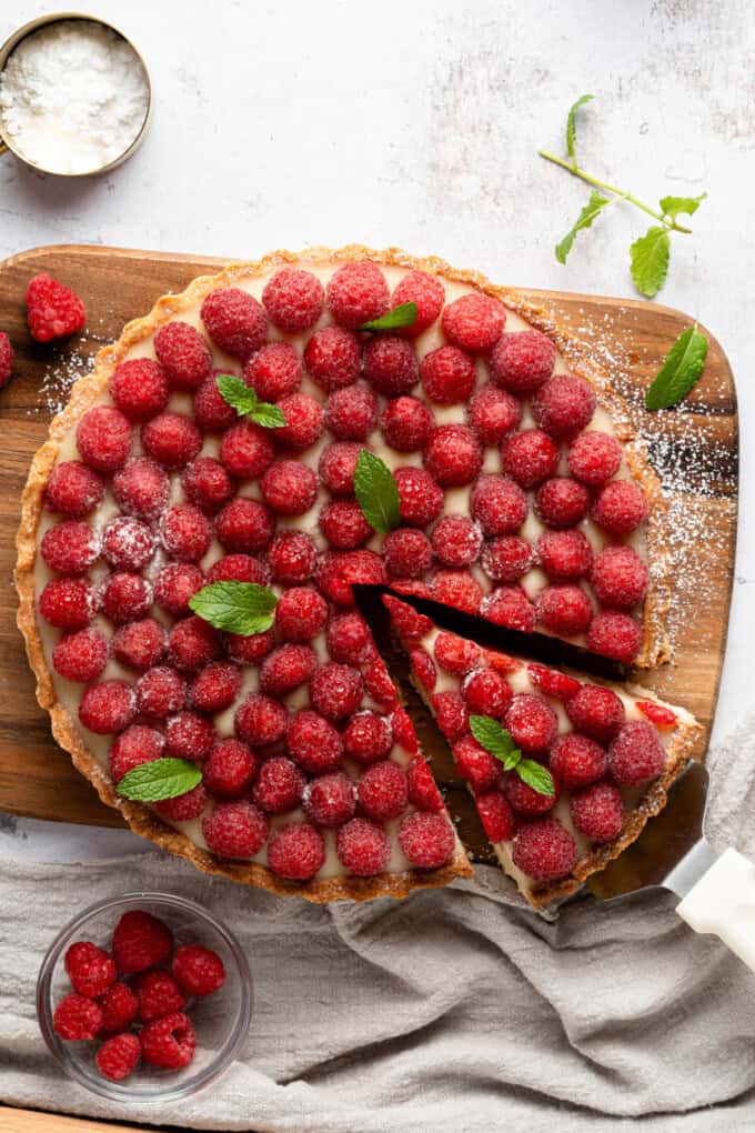 An overhead image of a raspberry chocolate tart with a slice being removed.