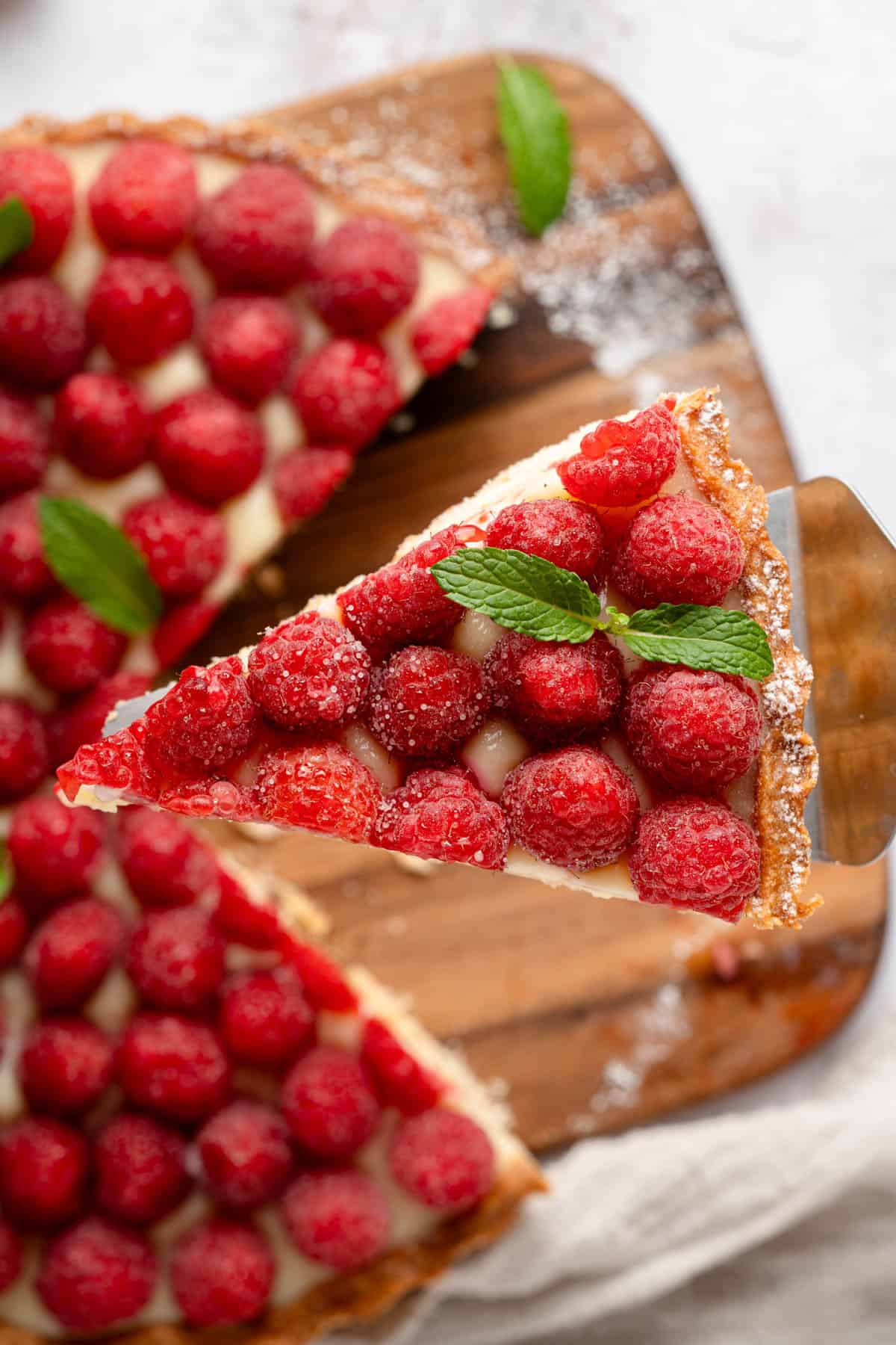 A slice of raspberry tart being held up over the rest of the tart.