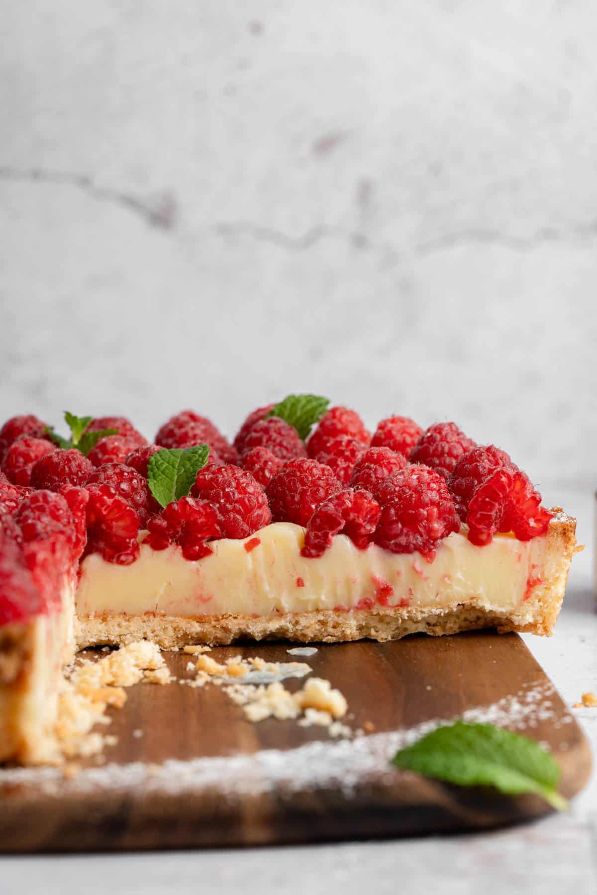 A side angle image of a white chocolate tart with fresh raspberries.