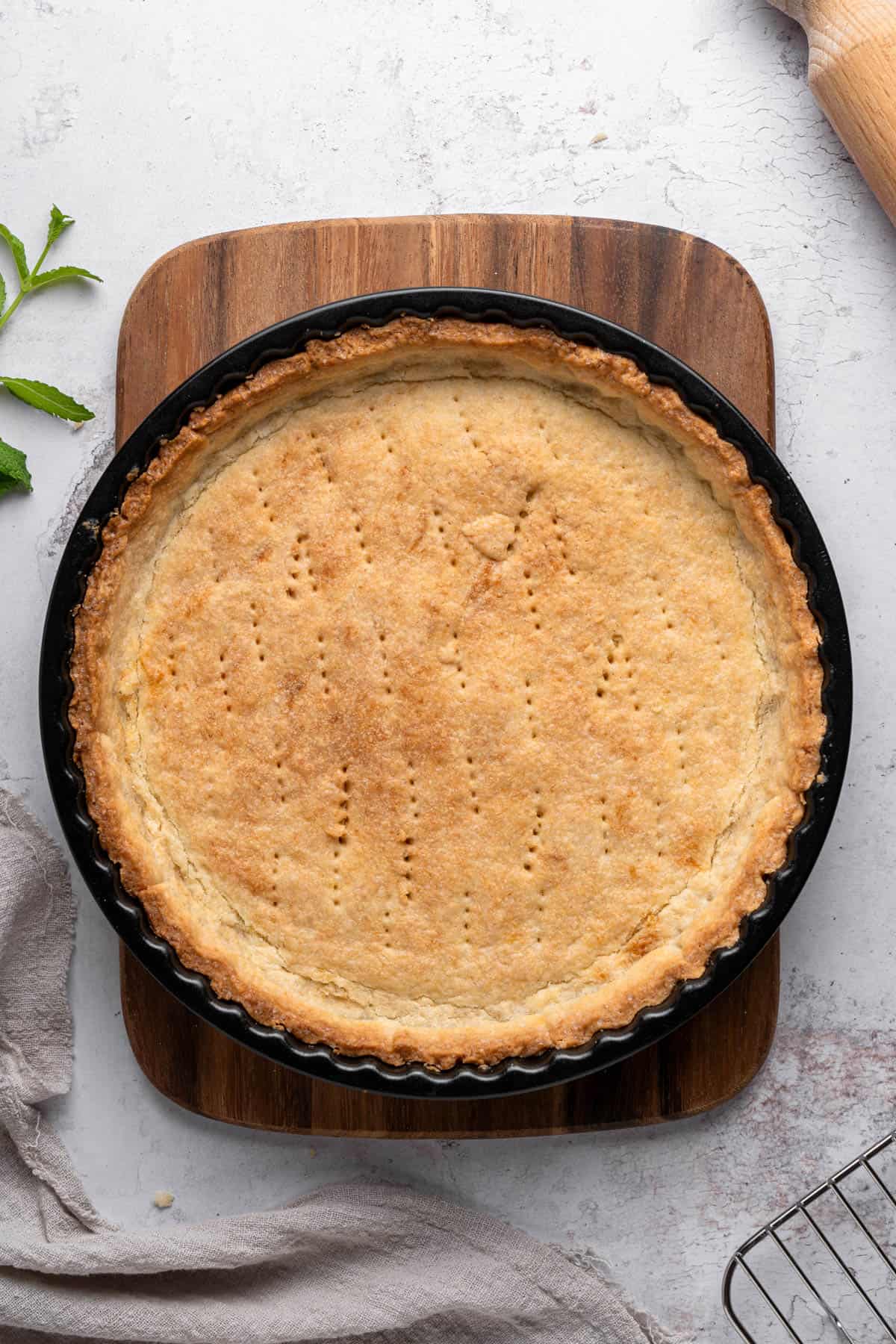 A baked tart shell on a wooden cutting board.