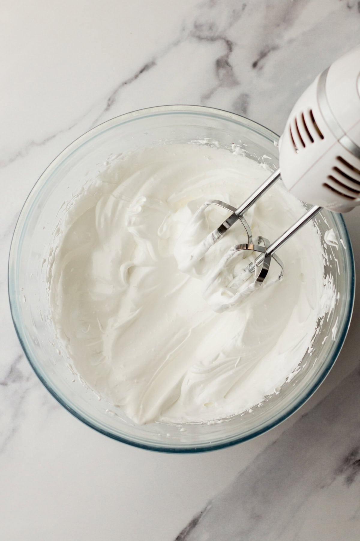 Beating meringue in a mixing bowl with a hand mixer.