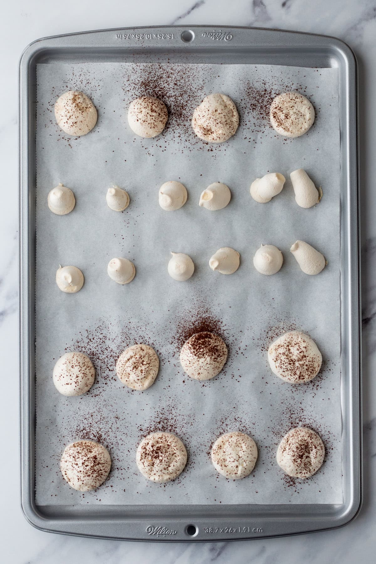 Baked meringue shapes dusted with cocoa powder on a baking sheet.