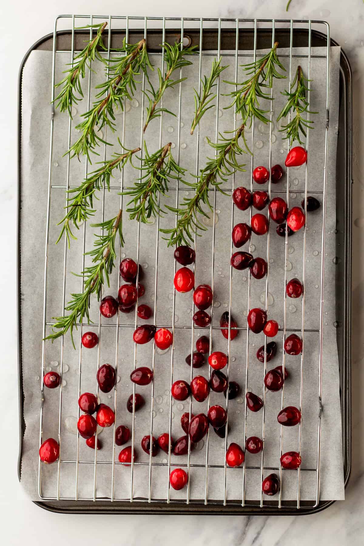 Letting cranberries and rosemary that have been soaked in simple syrup dry out on a wire rack over a baking sheet.