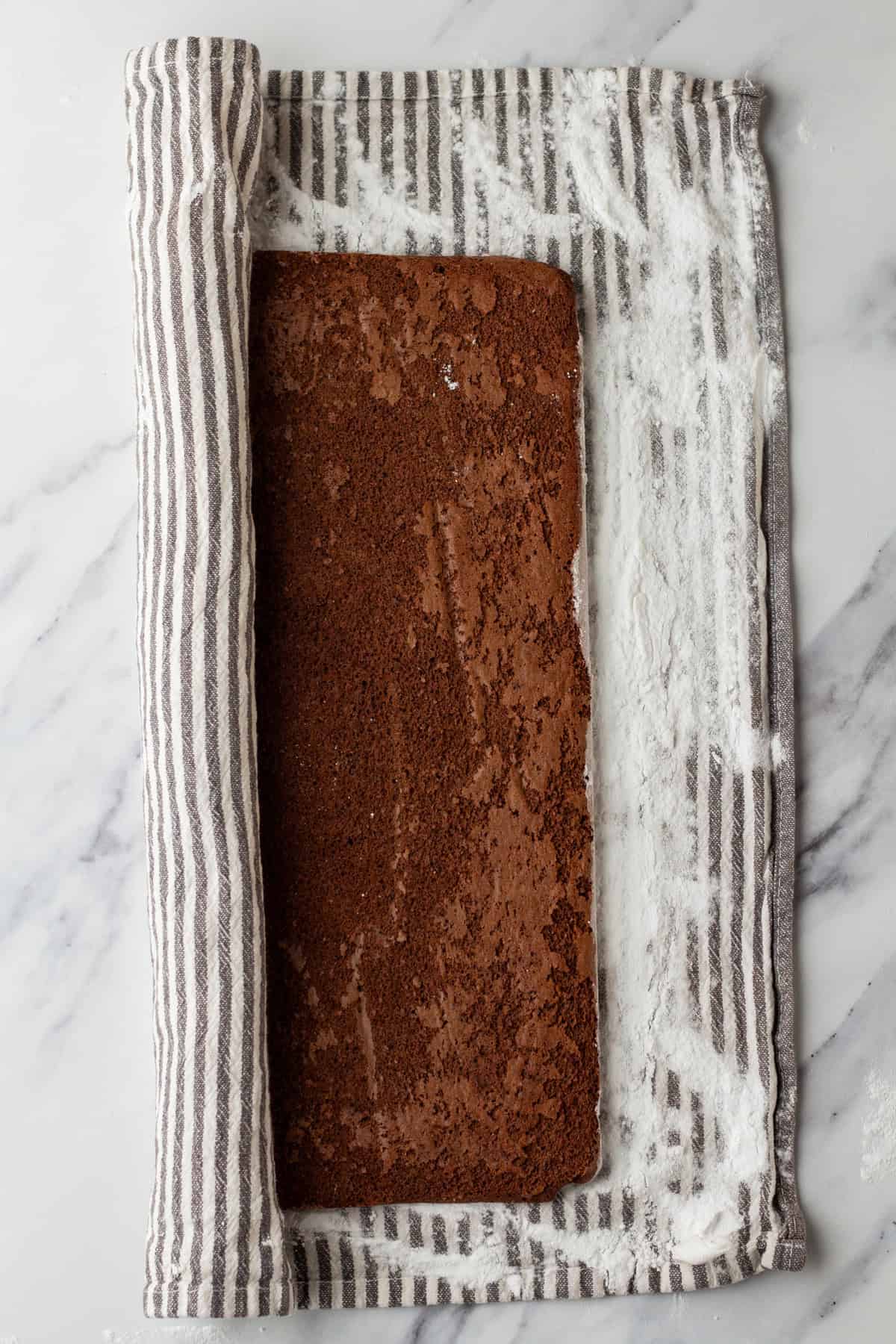 Rolling up a chocolate cake in a towel dusted with powdered sugar.