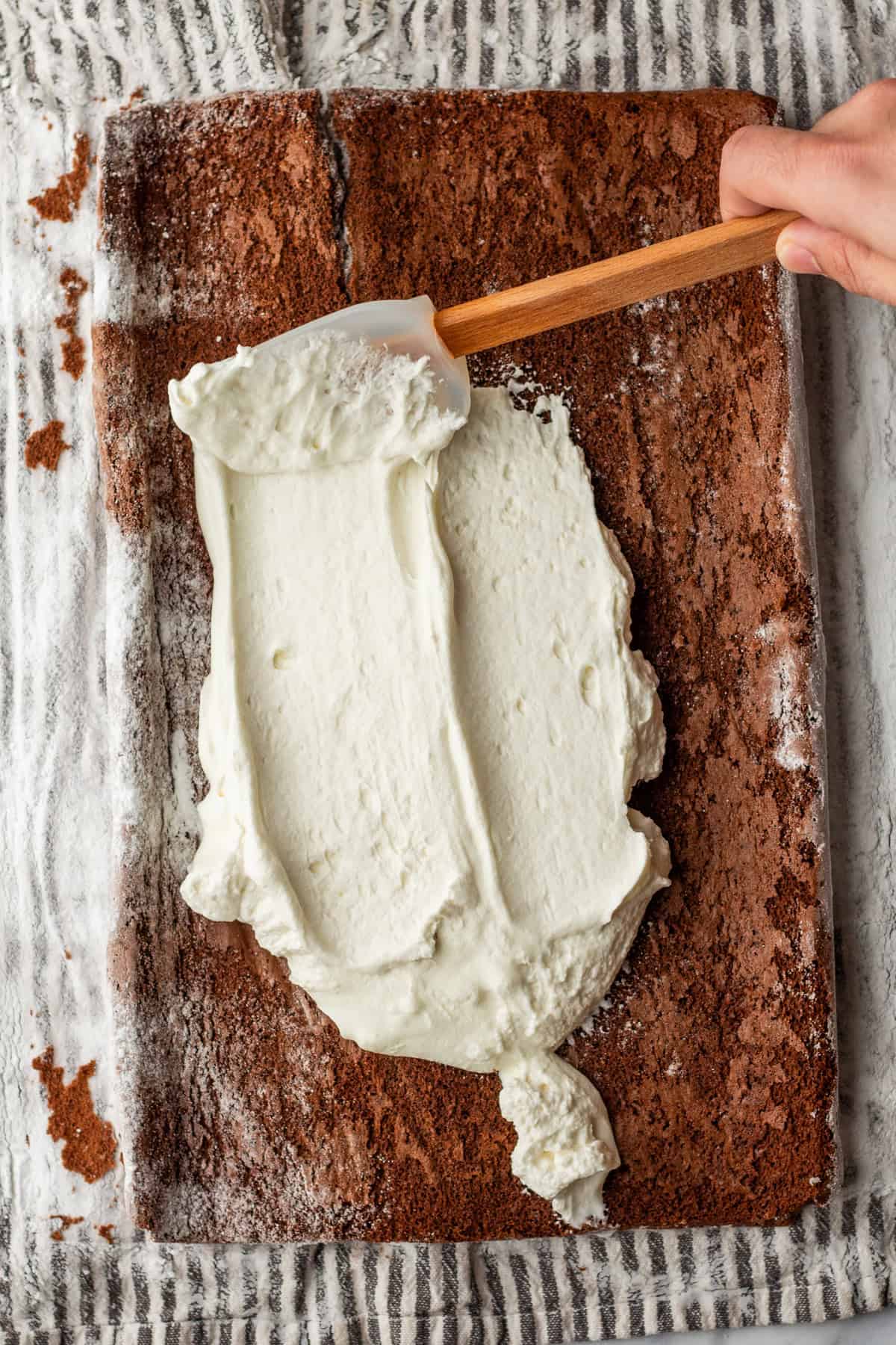 Spreading whipped cream over a cooled chocolate roll cake.