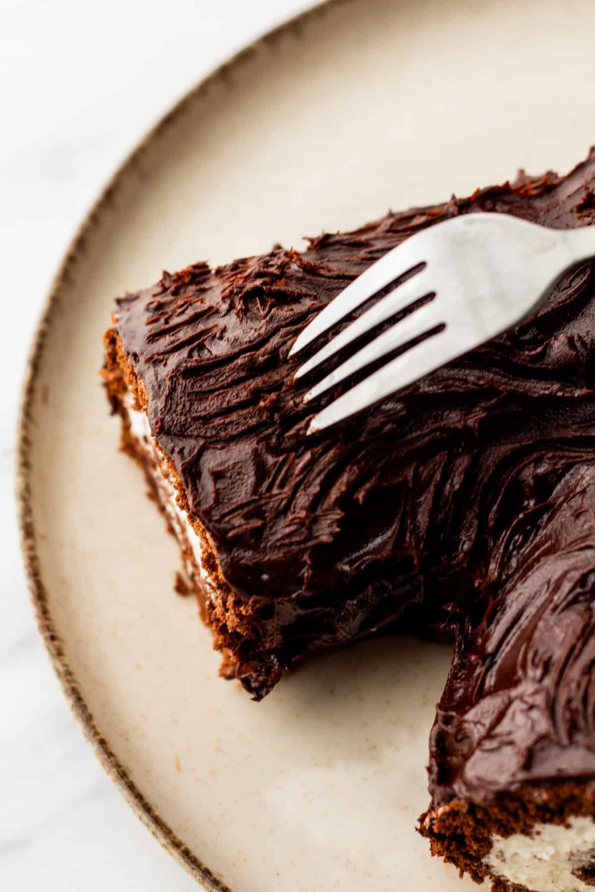 The tines of a fork being dragged through chocolate ganache to create lines on a yule log.