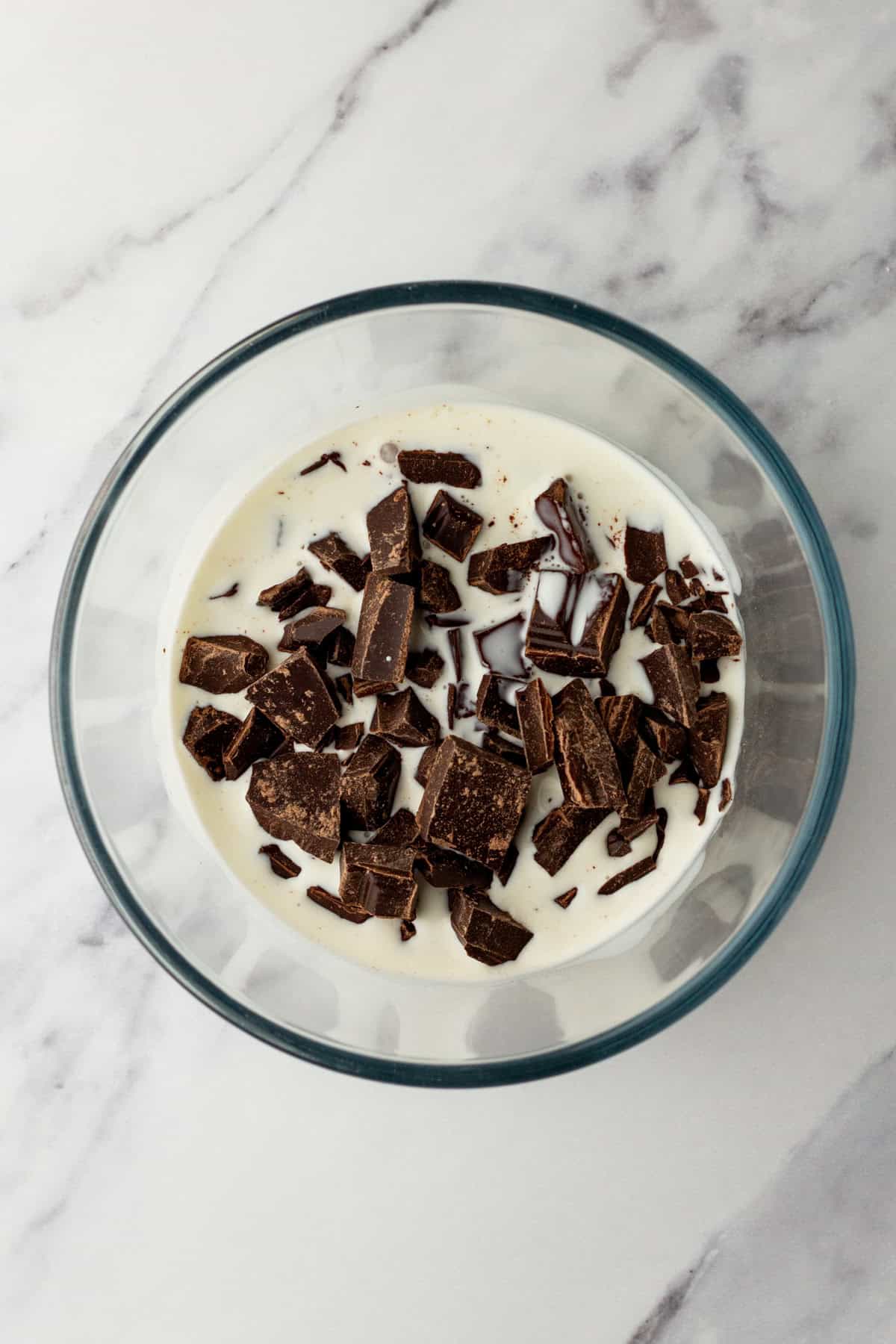 Letting hot cream and chopped chocolate sit in a bowl to make ganache.