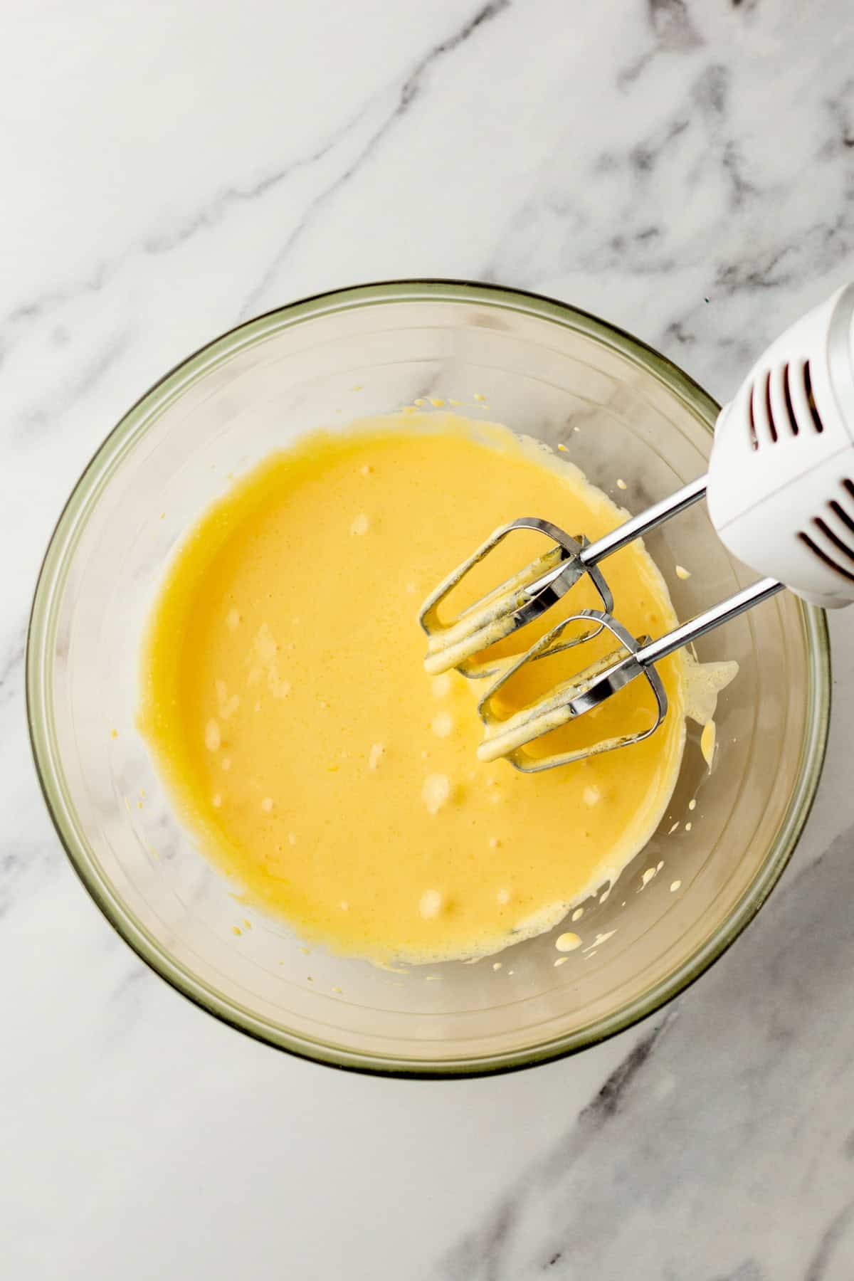 Beating sugar and eggs in a bowl with a hand mixer.