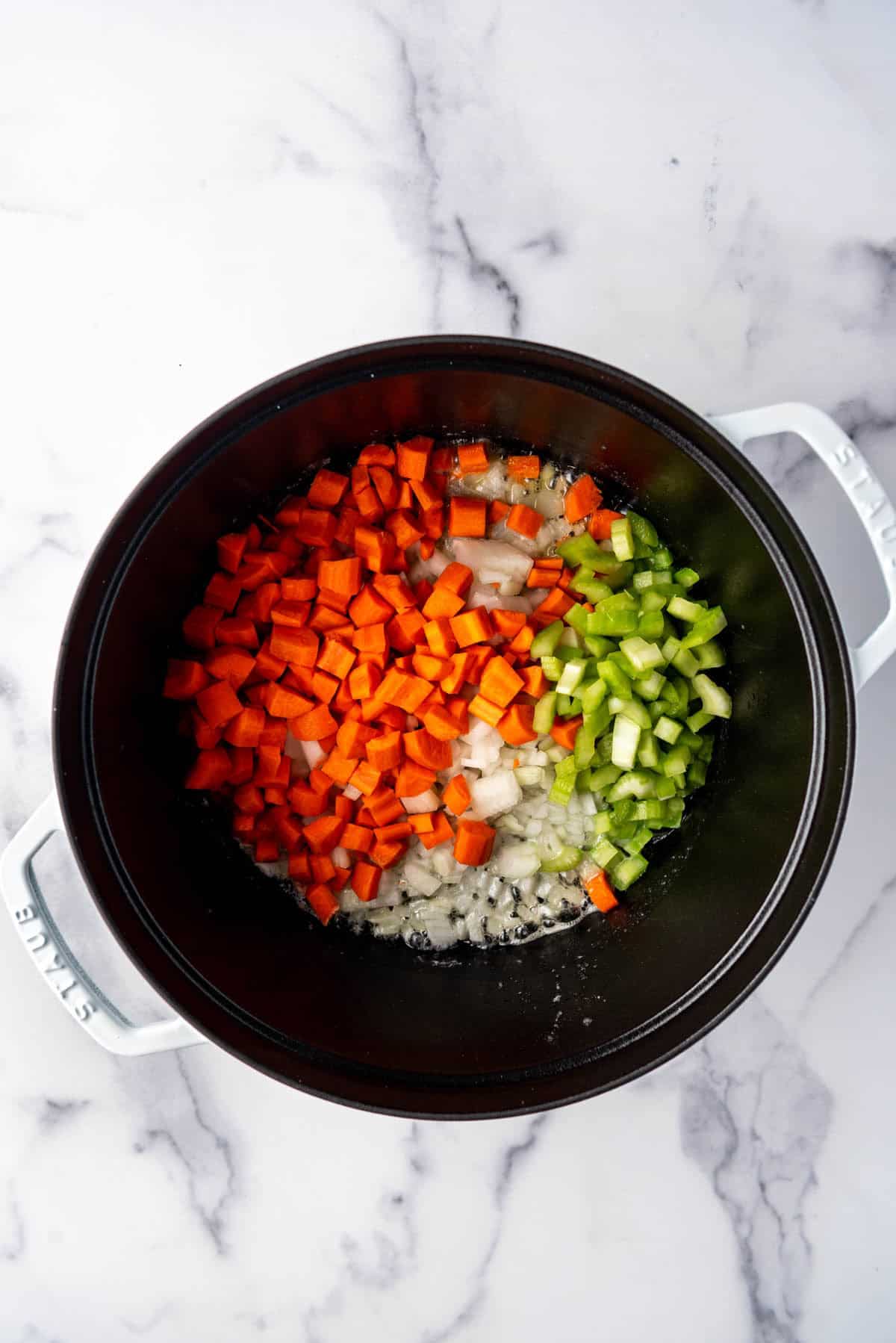 Adding chopped carrots, celery, and onions to melted butter in a dutch oven.