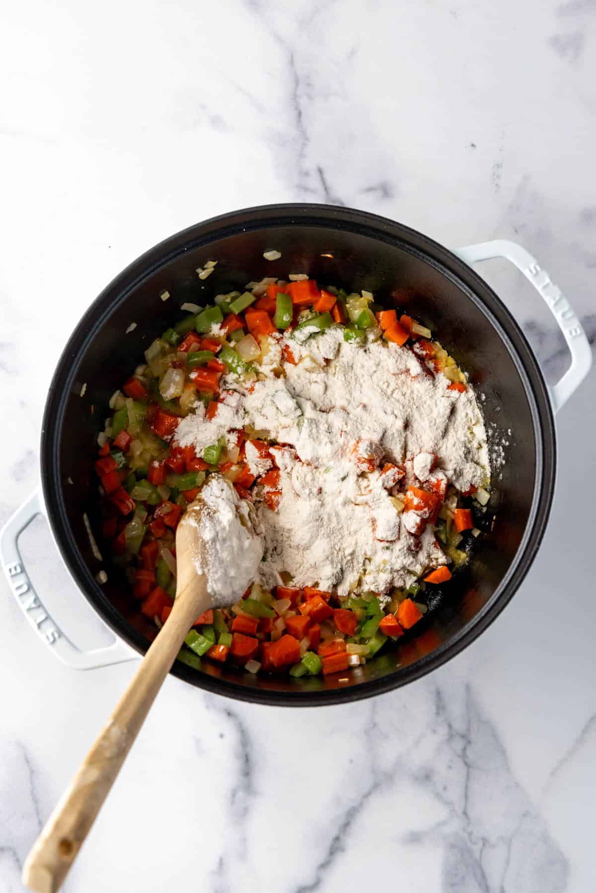 Adding flour to softened vegetables in a large pot.