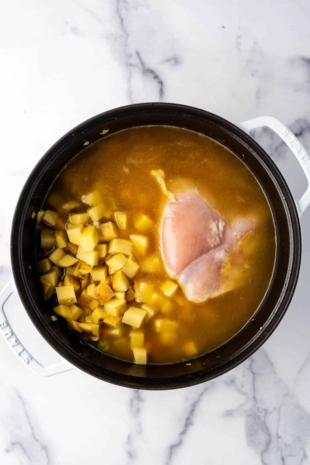 Adding potatoes, broth, and chicken breasts to a large pot.