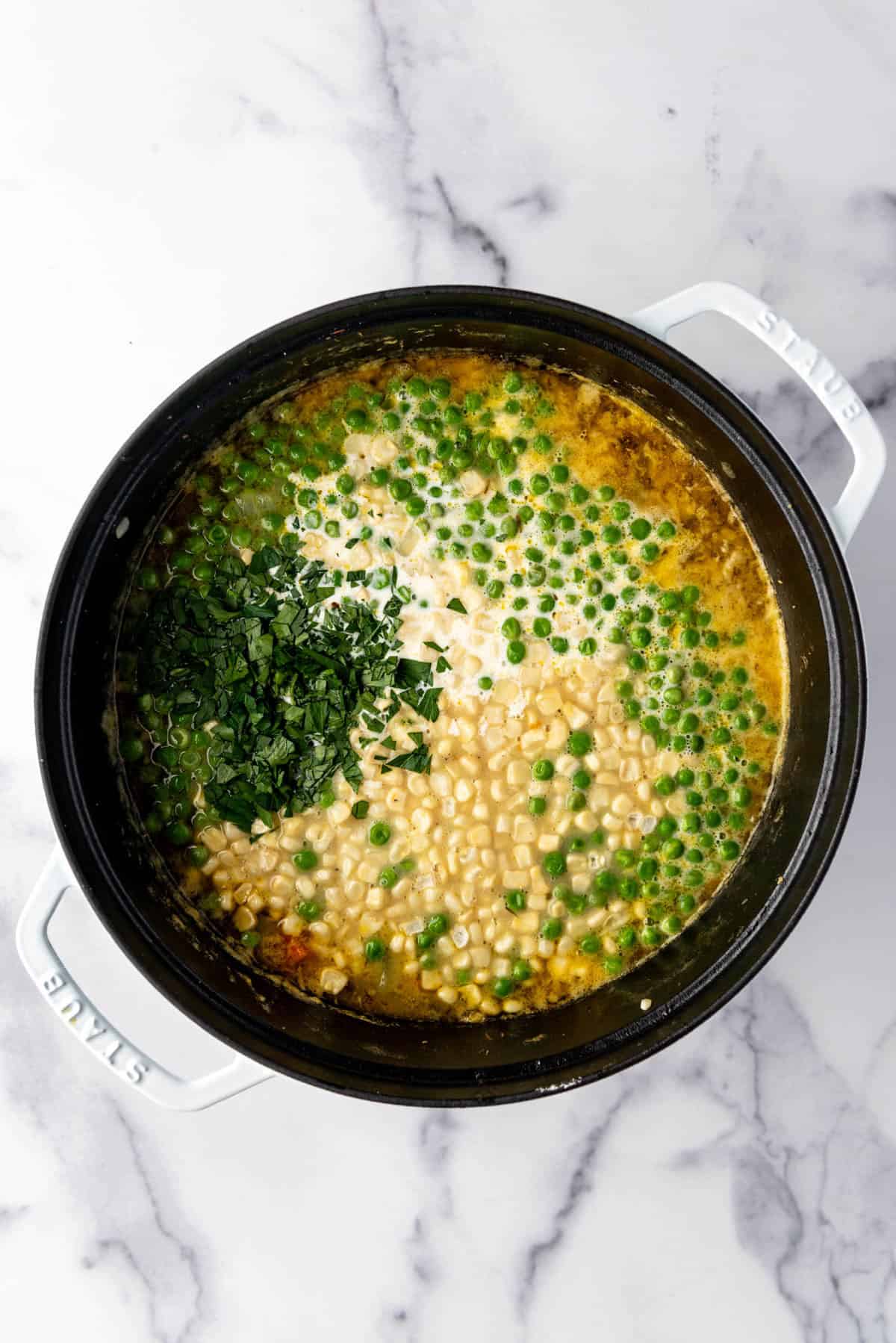 Adding corn, peas, herbs, and chopped parsley to a pot of soup.