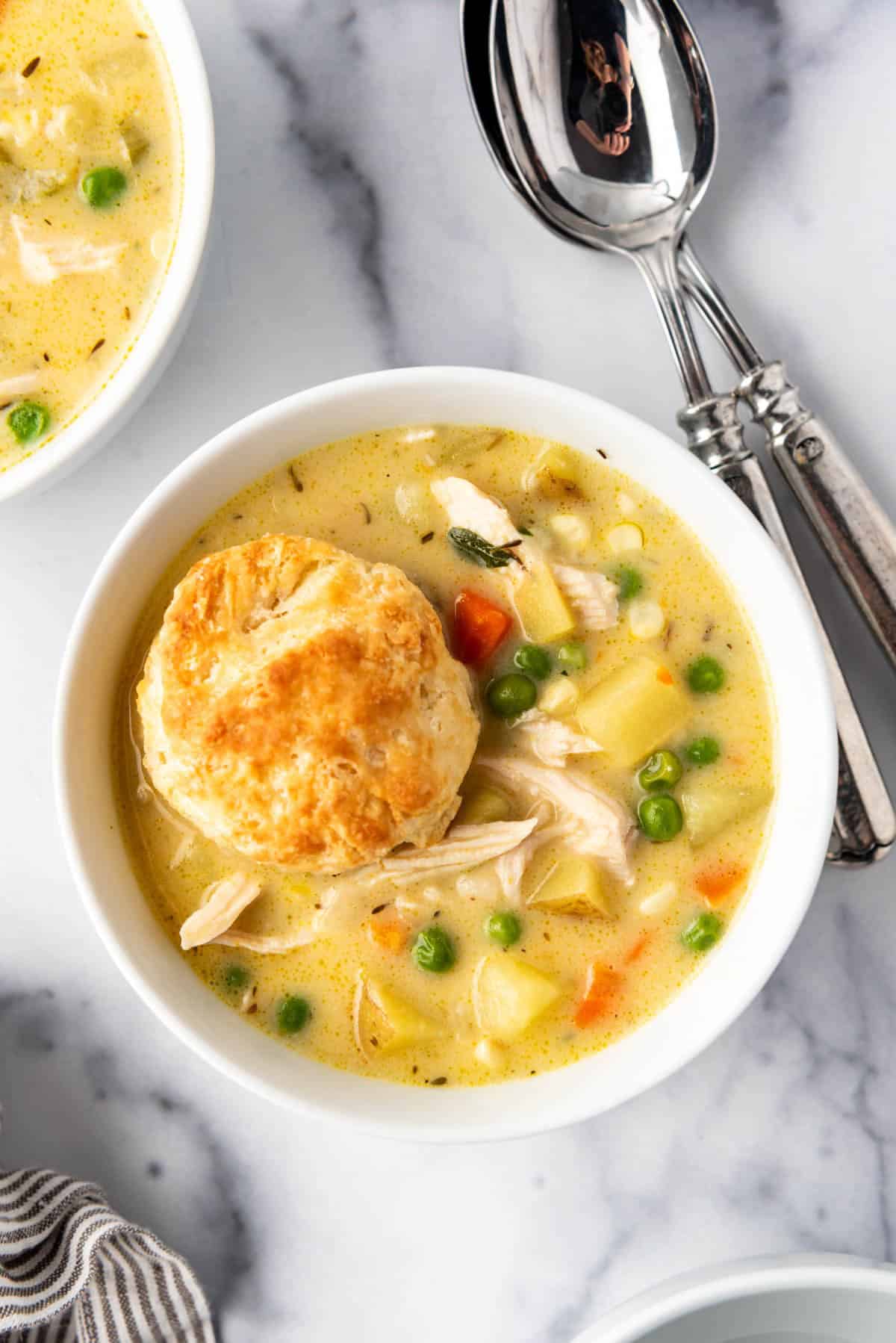 A close image of a bowl of chicken pot pie soup with a biscuit in it.