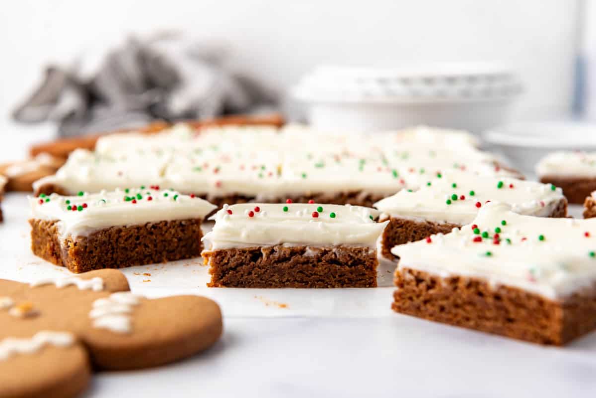 Gingerbread cookie bars with cream cheese frosting on a white surface.