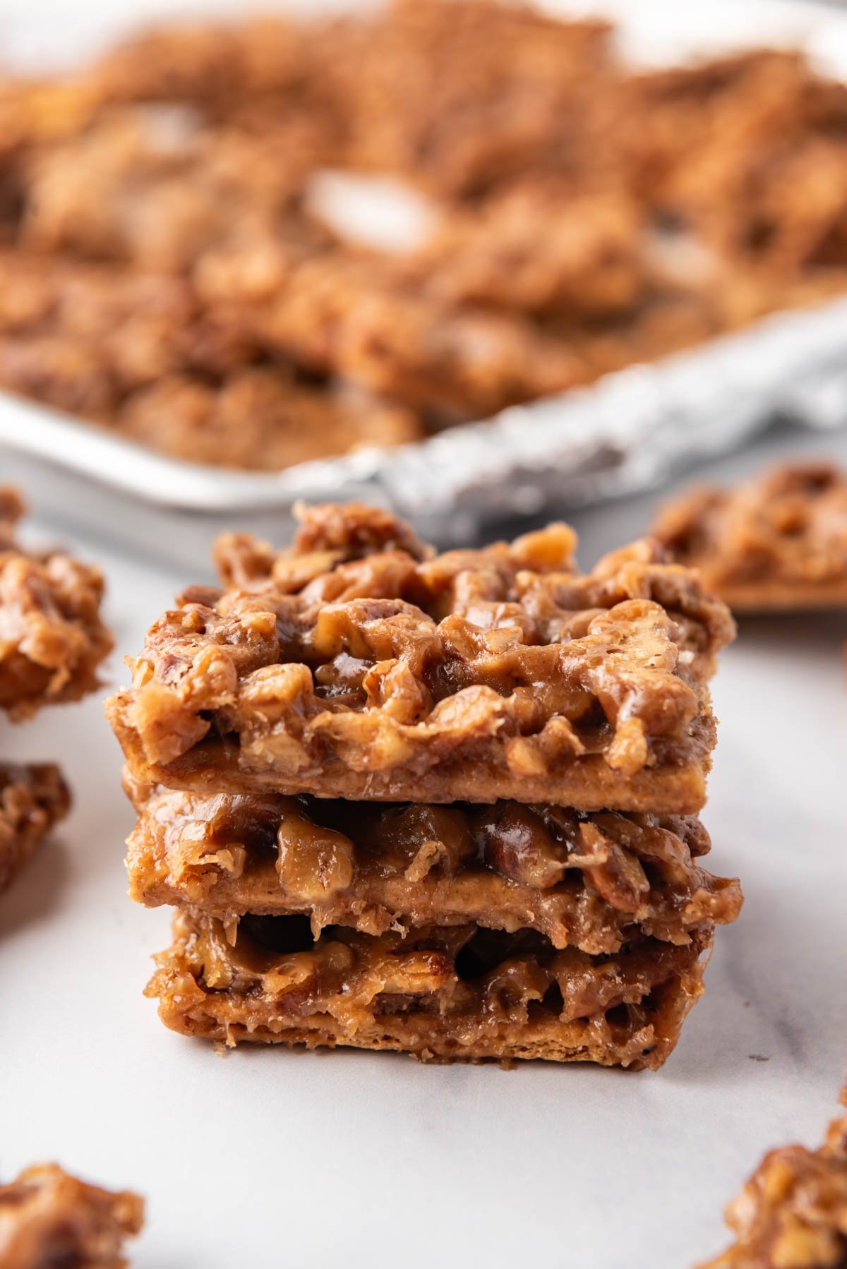 An image of a stack of pecan pie bark in front of a baking sheet with more bark on it.