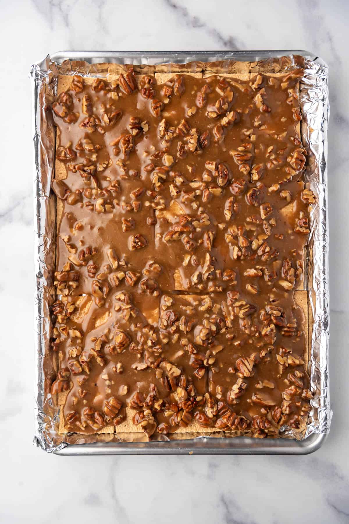 Pecan pie filling poured over graham crackers on a baking sheet lined with aluminum foil.