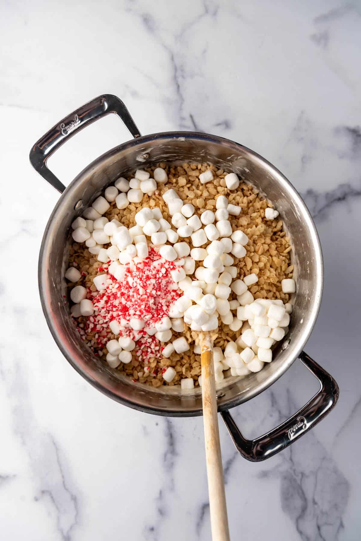 Adding reserved marshmallows, rice krispies and crushed candy canes to a large pot.