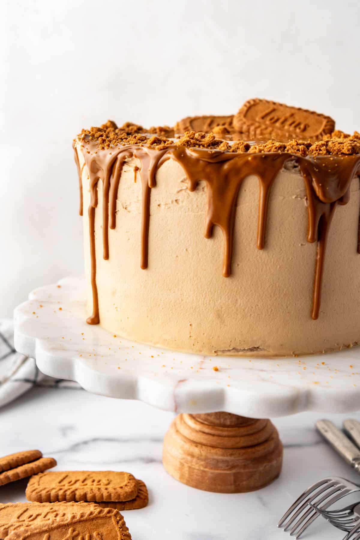 A side view of a homemade Biscoff cookie butter cake on a white marble cake stand with a wooden base.