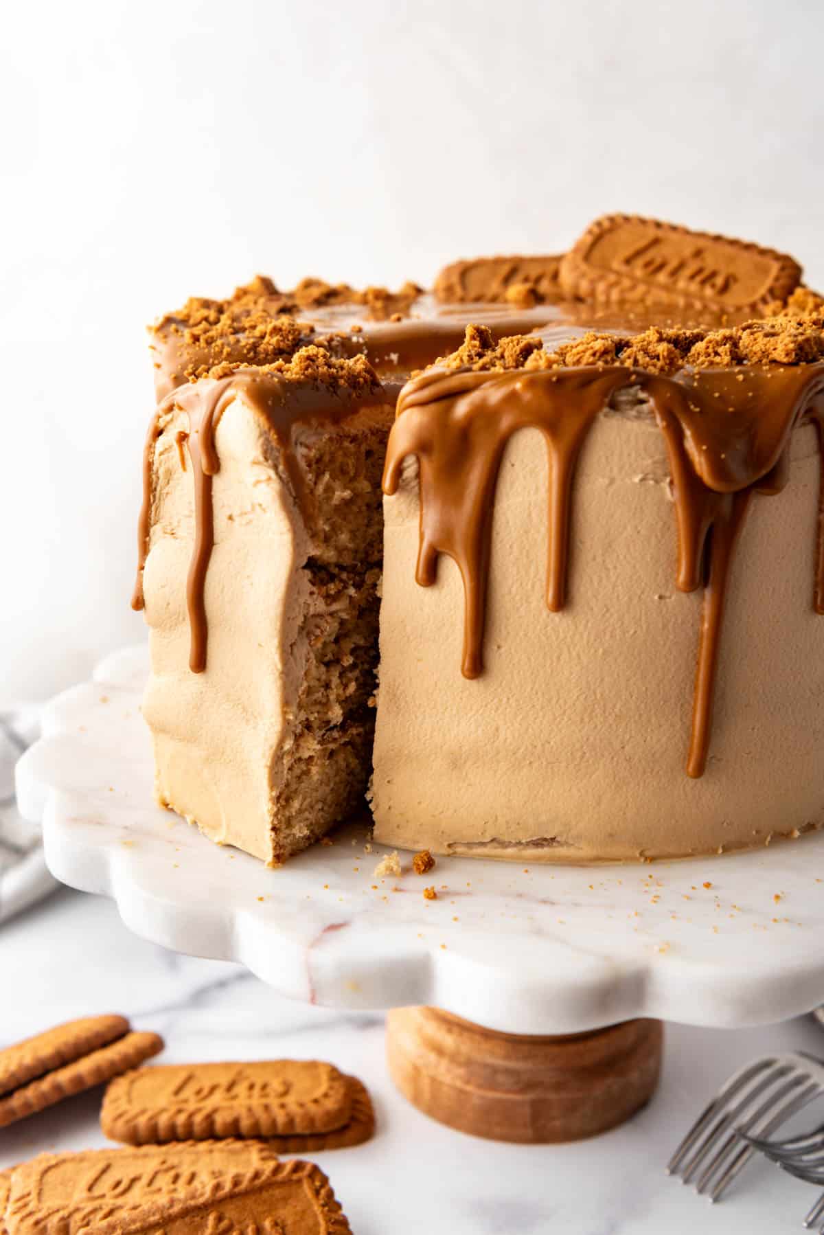 A biscoff cookie butter cake on a white cake stand with biscoff cookies in front of it.