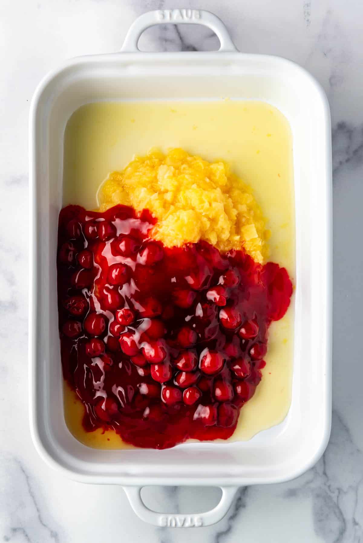 Combining cherry pie filling and crushed pineapple in a large baking dish.