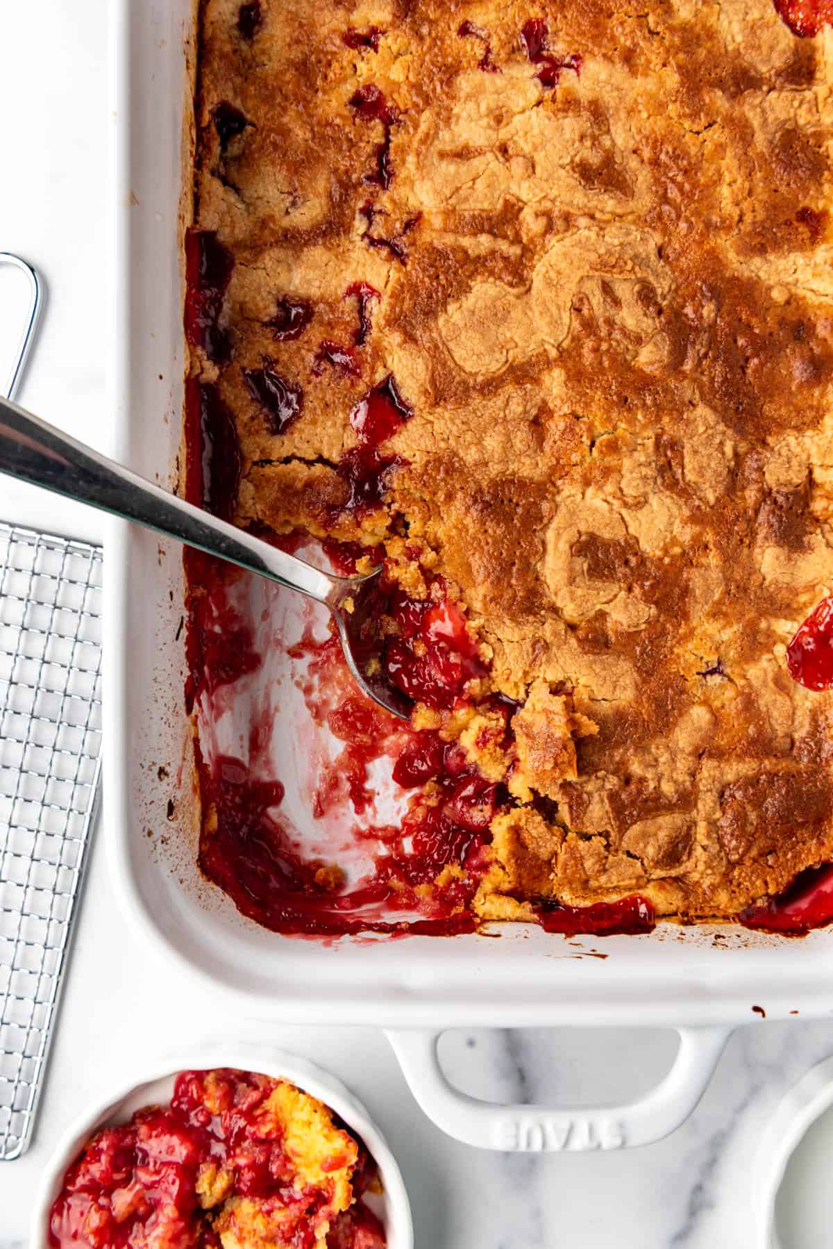 An overhead image of a dump cake with cherries and pineapple with a scoop removed.