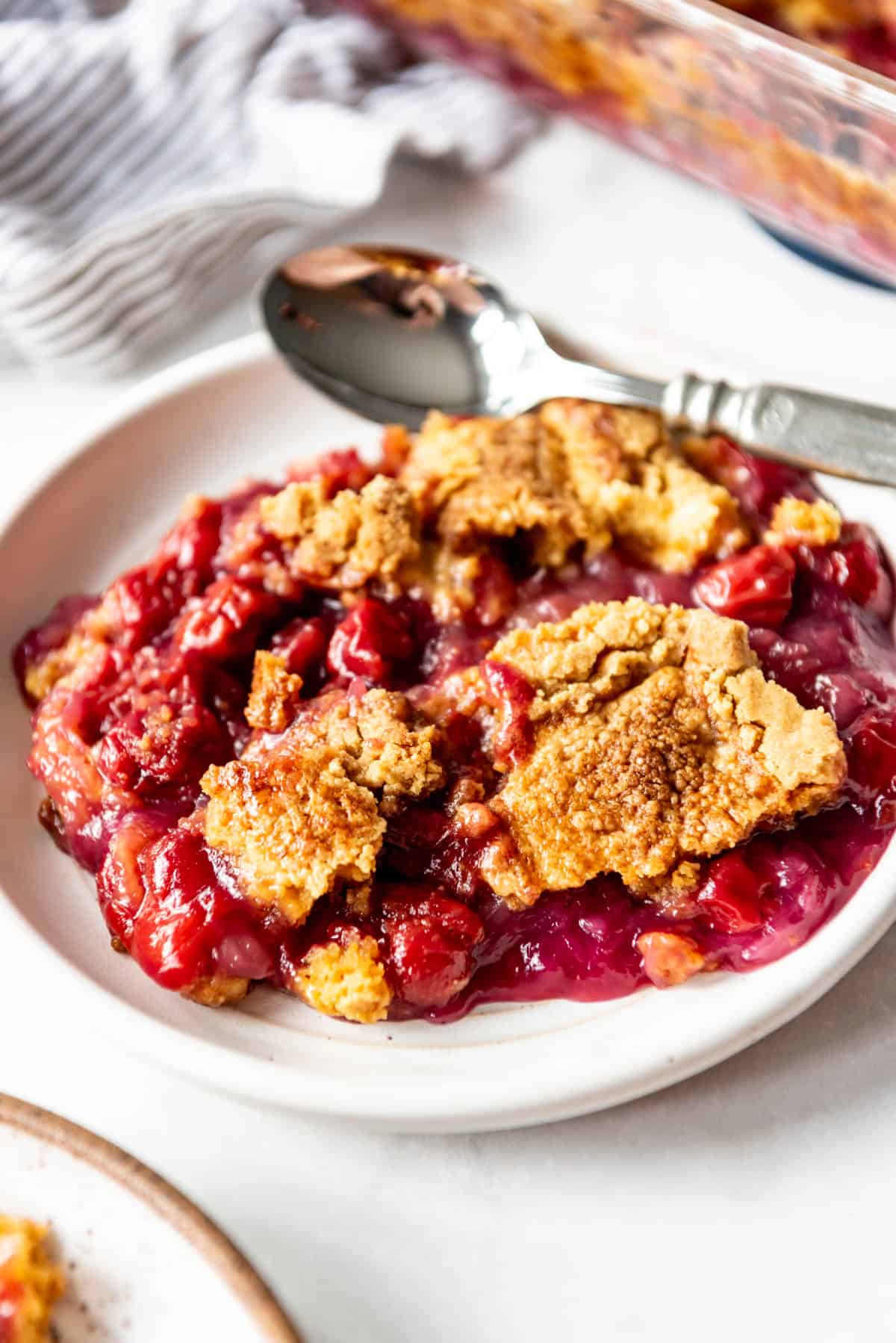 A large plate of cherry pineapple dump cake with a spoon on it.