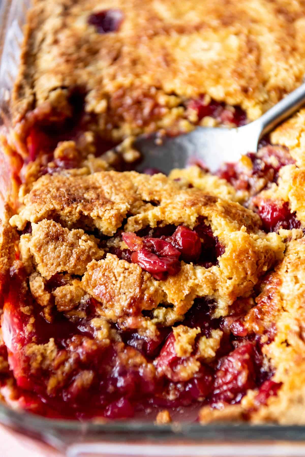 A close up image of a scoop of cherry pineapple dump cake with a serving spoon.